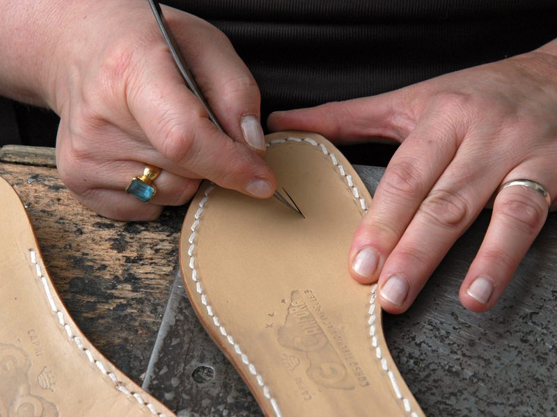 An artisan's hands tooling a stitched leather sole