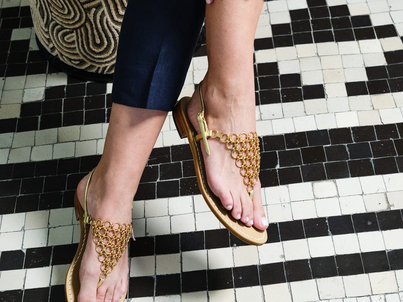 Gold sandals with a woven chain upper, worn on a mosaic floor